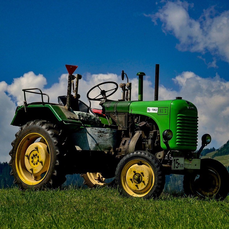 Traktor auf einer grünen Wiese vor Bergpanorama